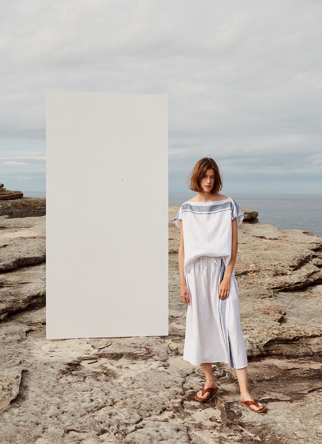 A square-cut, boatneck, easy-fit top with cap sleeves that has a longer length at the back made from yarn dye stripe washed linen in white with indigo stripe