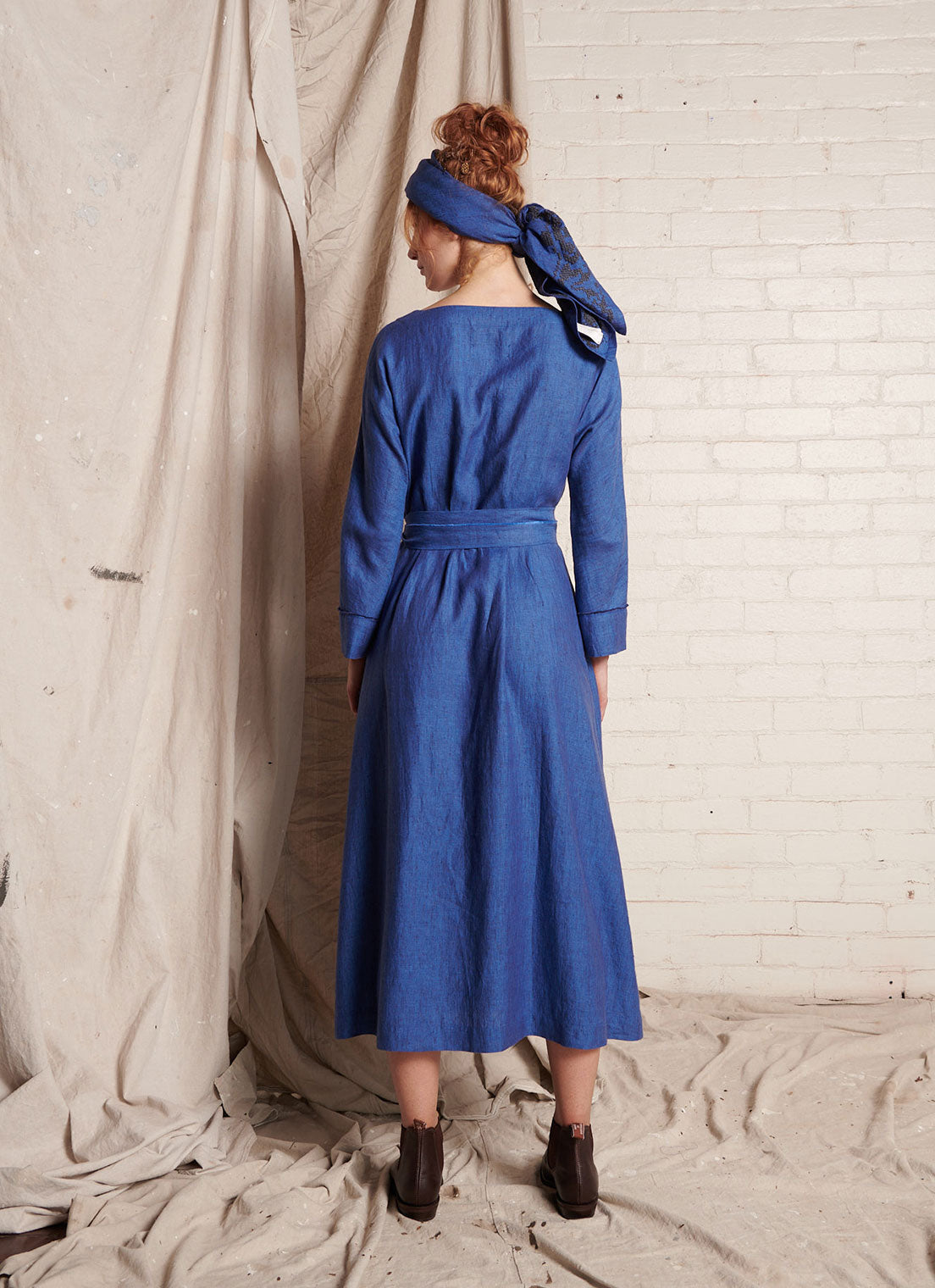 A blue, wrap, midi-length dress with open, square-cut neckline and long, cuffed sleeves with hand frayed edge finish made from European linen