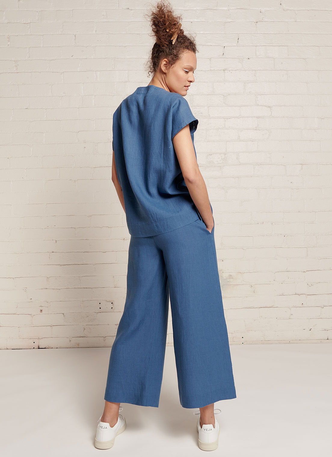 An indigo, loose fitting crop pants with elasticated waistband and tie belt of the same fabric made from yarn dye washed linen