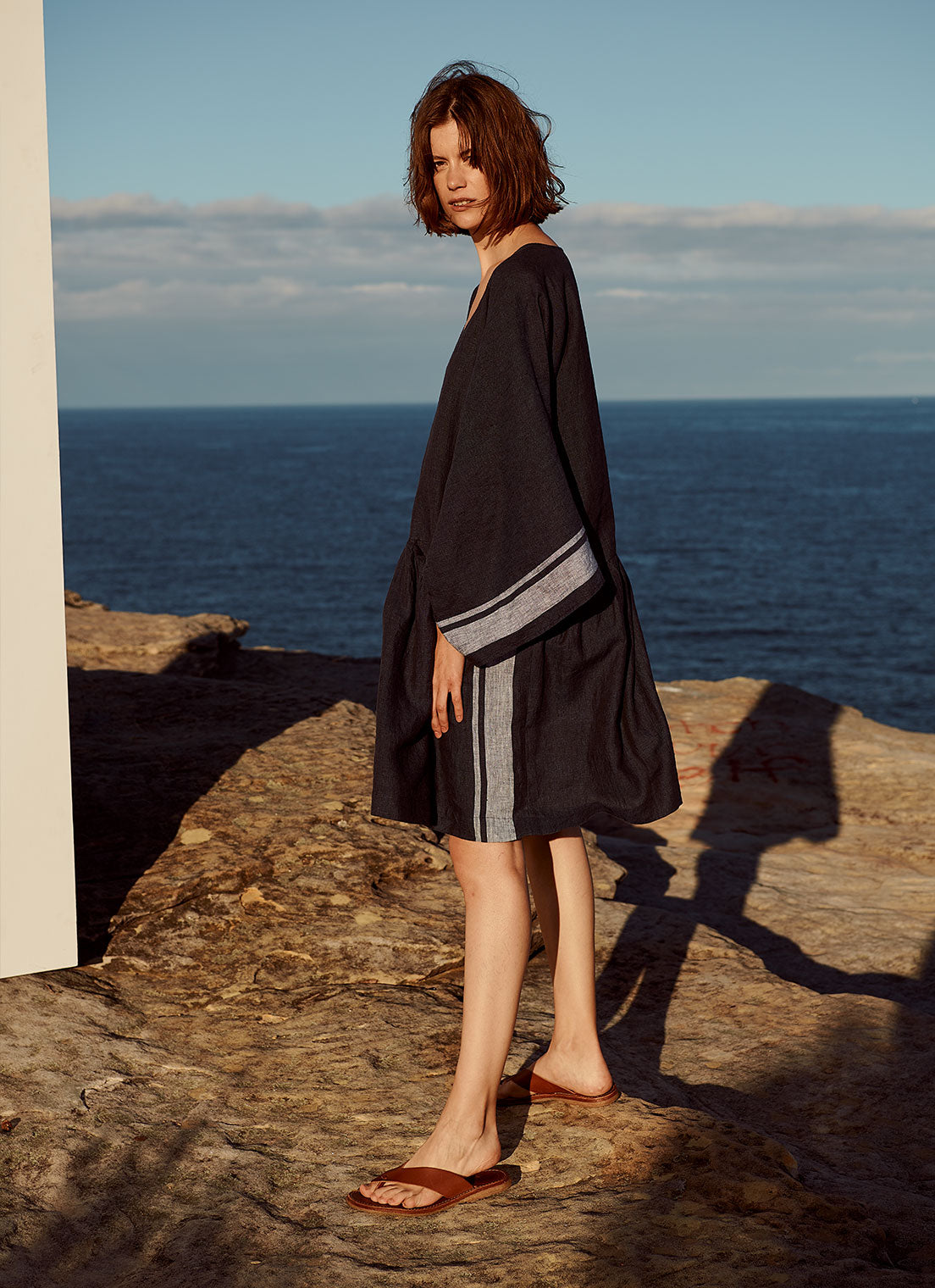 A relaxed, V-neck, gathered dress with pockets and long, loose sleeves made from yarn dye stripe washed linen in ink with pale blue stripe