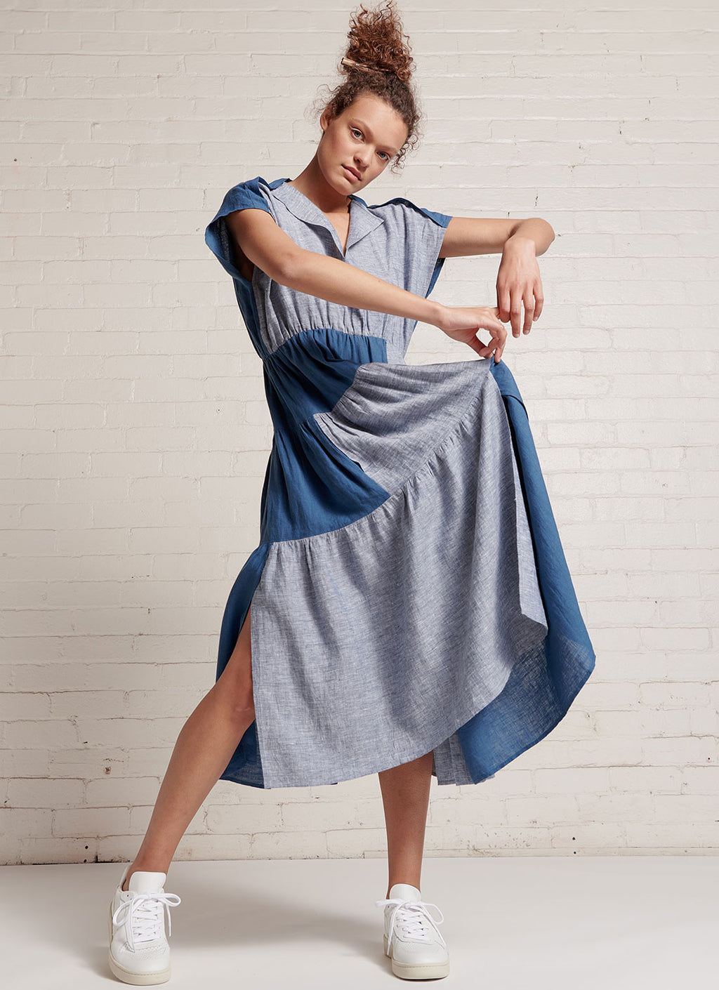 An indigo and denim two-tone, patchwork, midi tiered dress with capped sleeves, pleated detail on the neckline and at the back, elastic waist and slits on the skirt made from yarn dye washed linen