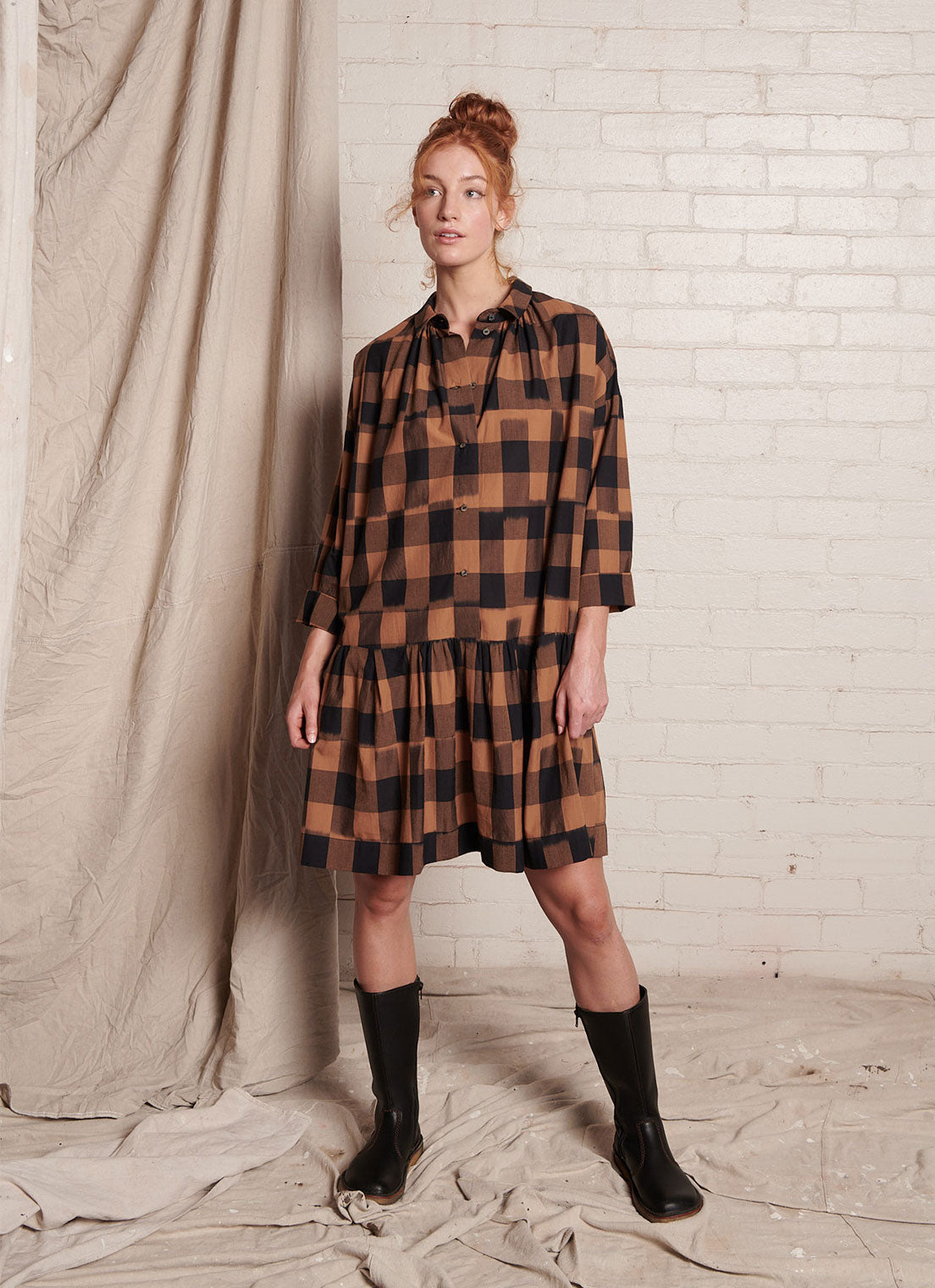 A bronze plaid, knee-length dress with centre front button fastening, collared neckline and gathered details from the hip made from handwoven ikat cotton