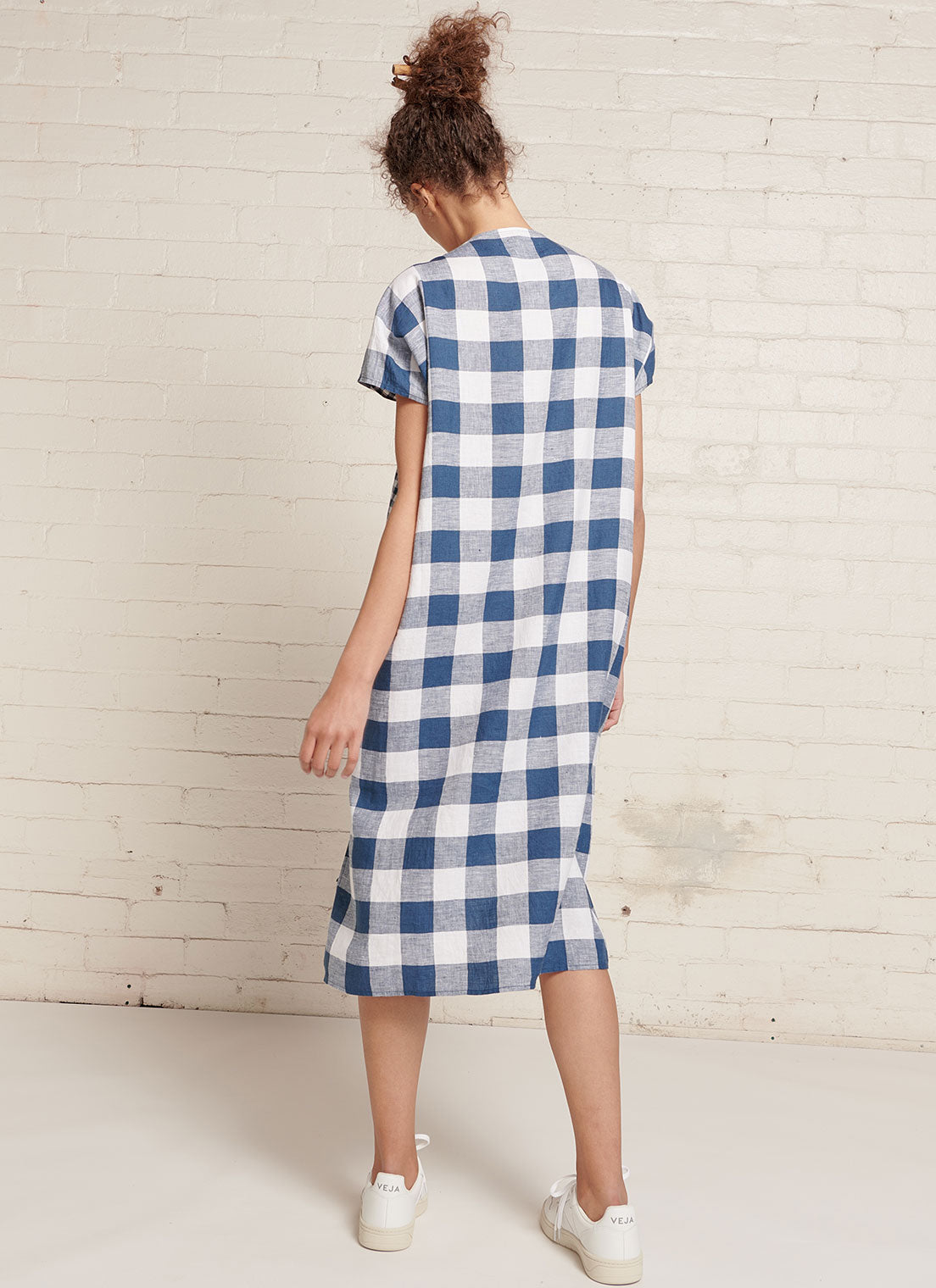 An indigo and white gingham linen dress with short sleeves, open neckline and centre front pleat detail made from mixed gingham yarn dye washed linen
