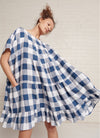 An indigo and white gingham, easy fit, knee-length, tiered dress with round neckline, short sleeves, tie closures at the back made from large gingham yarn dye washed linen