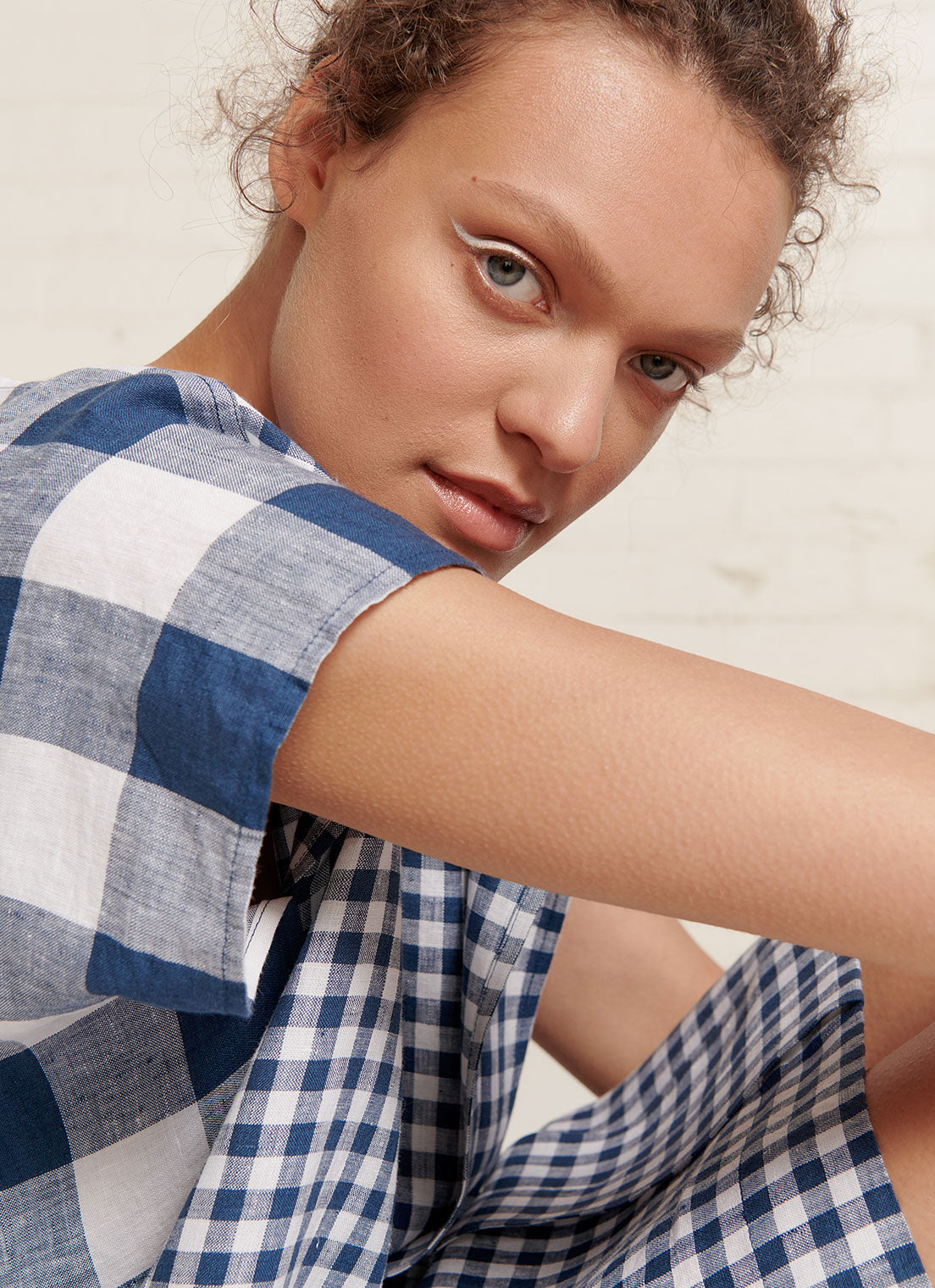 An indigo and white gingham linen dress with short sleeves, open neckline and centre front pleat detail made from mixed gingham yarn dye washed linen