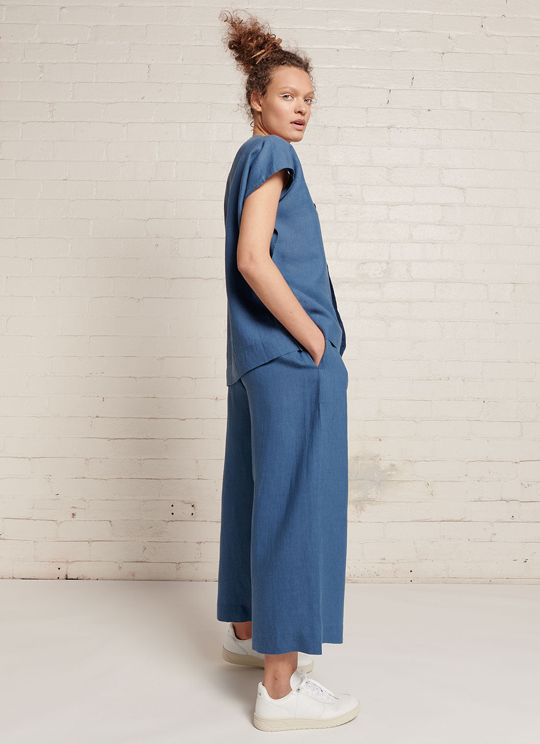 An indigo, loose fitting crop pants with elasticated waistband and tie belt of the same fabric made from yarn dye washed linen