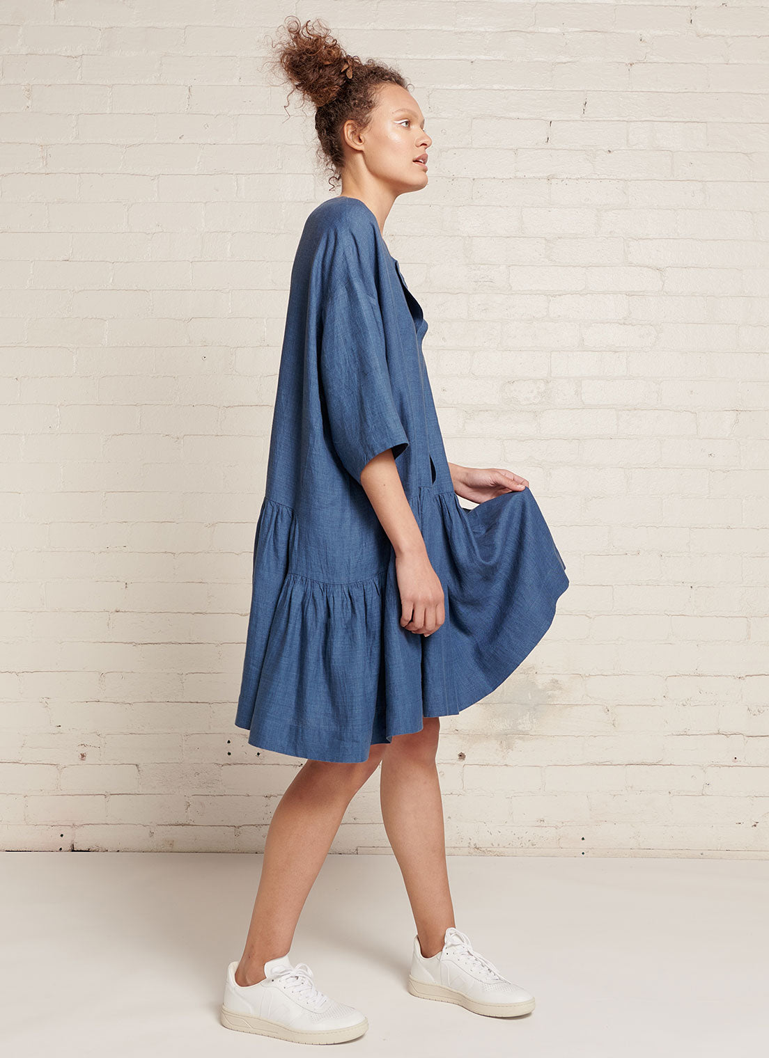 An indigo, easy fit, knee-length, square-cut dress with open neckline, 3/4 sleeves, and gathered detailing made from yarn dye washed linen