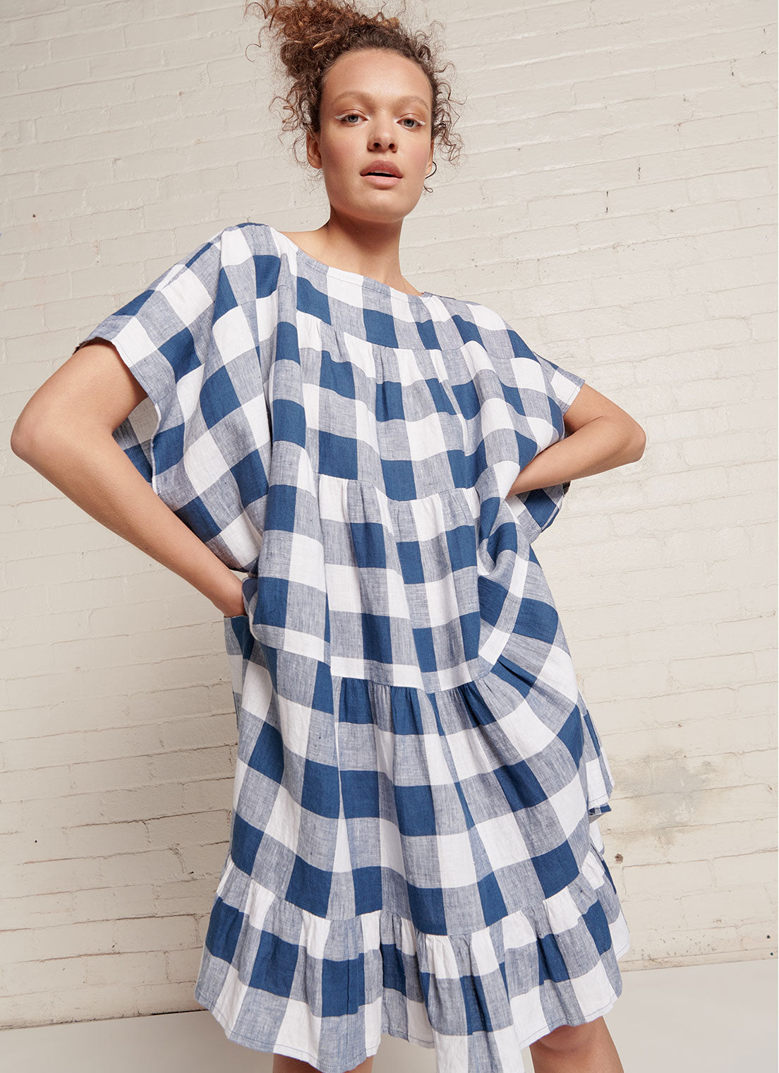 An indigo and white gingham, easy fit, knee-length, tiered dress with round neckline, short sleeves, tie closures at the back made from large gingham yarn dye washed linen