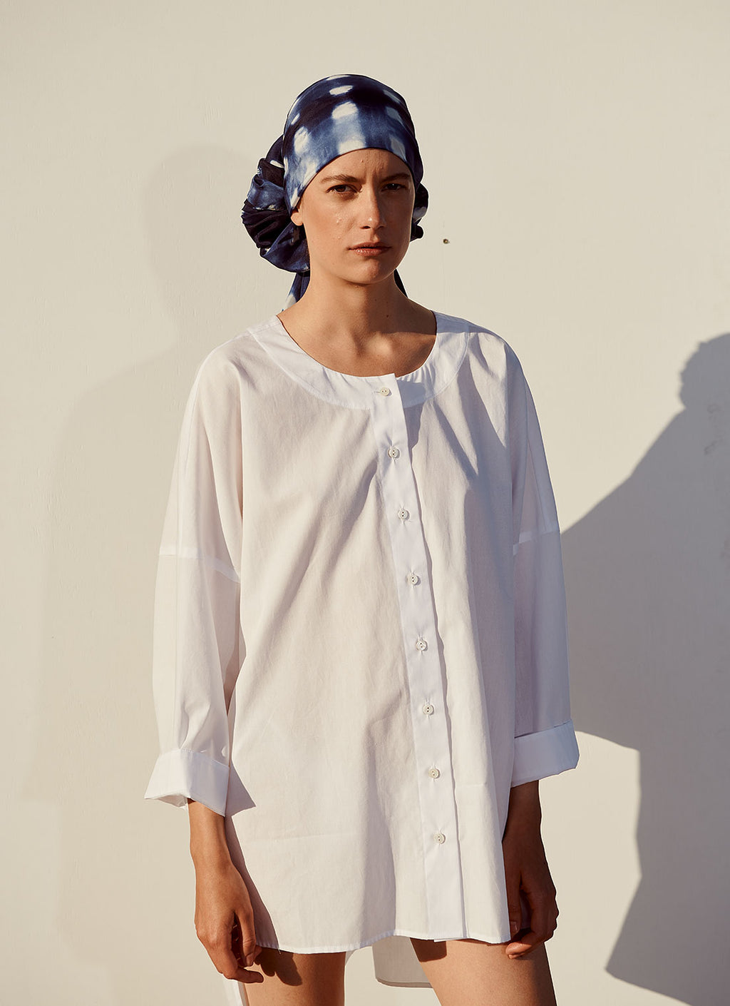 An easy fit, round neck, button-up, white cotton blouse with ¾, loose sleeves, has longer length and twist detail at the back