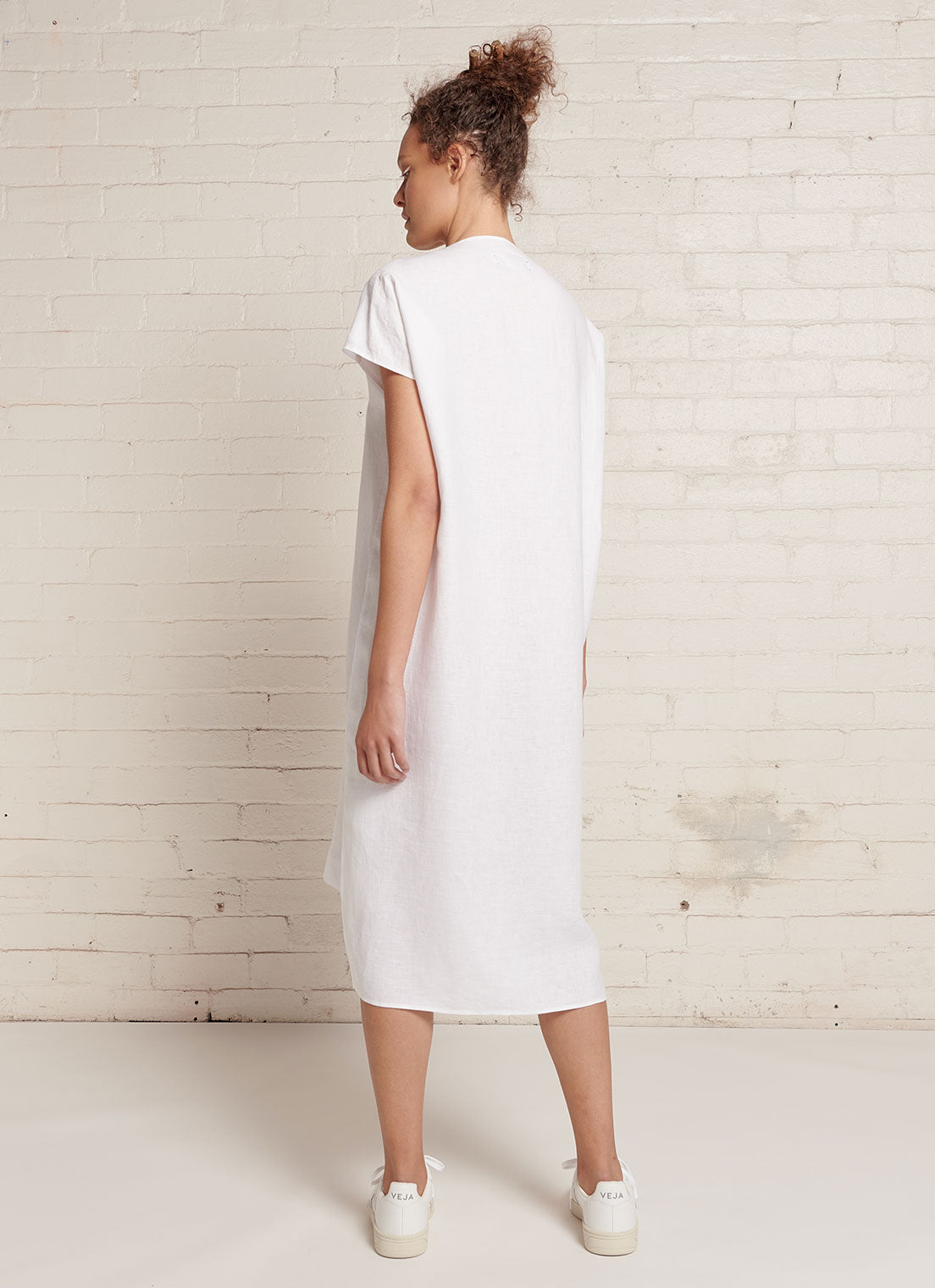 A white, knee-length linen dress with short sleeves, open neckline and centre front pleat detail made from yarn dye washed linen