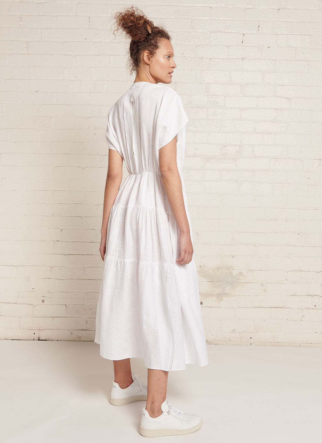 An white, midi tiered dress with capped sleeves, pleated detail on the neckline and at the back, elastic waist and slits on the skirt made from yarn dye washed linen